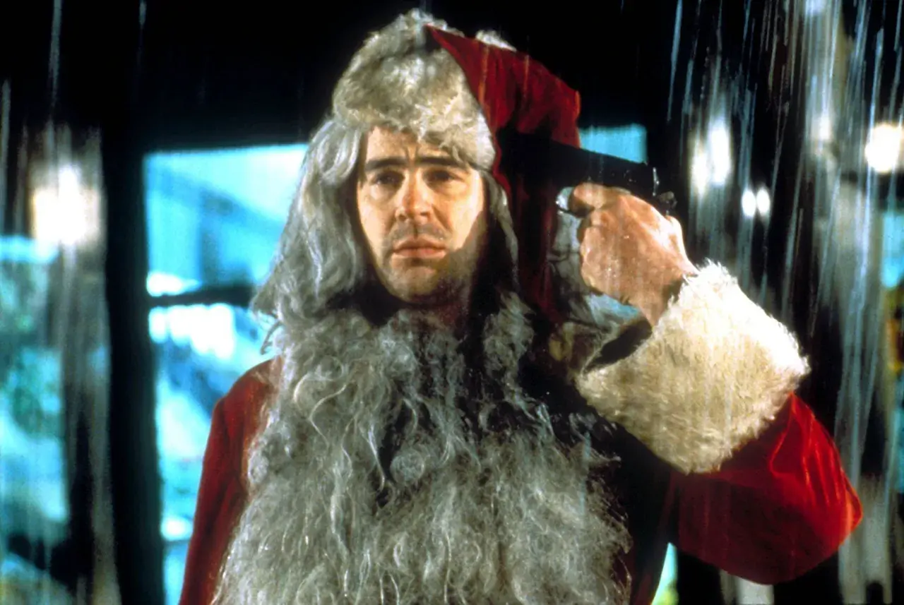 Un uomo con barba e cappello da Babbo Natale tiene una pistola puntata alla tempia. Sembra una scena da "Una poltrona per due Babbo Natale".