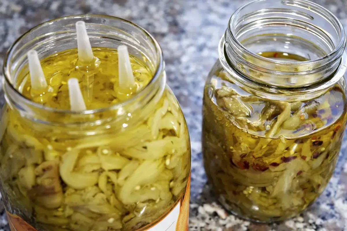 Due barattoli di melanzane a filetti sott'olio, uno con quattro tappi bianchi che emergono dall'olio dorato.