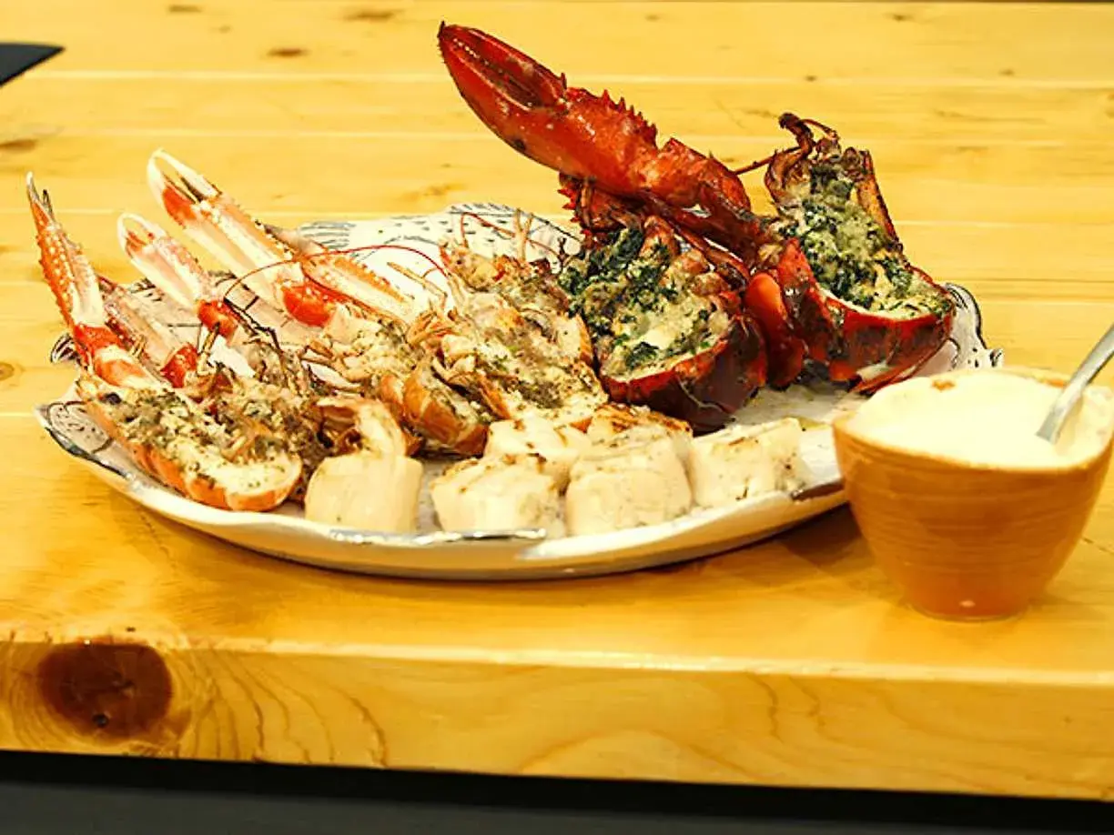 En tallrik med grillade skaldjur, inklusive hummer och havskräftor, serveras med en skål dippsås.
