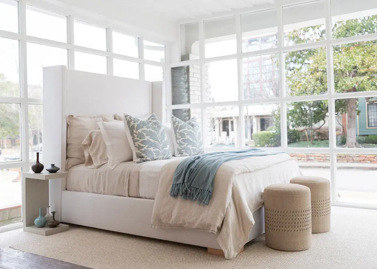 A light blue throw with fringe adds a cozy touch to this serene bedroom, draped over a bed with linen bedding.