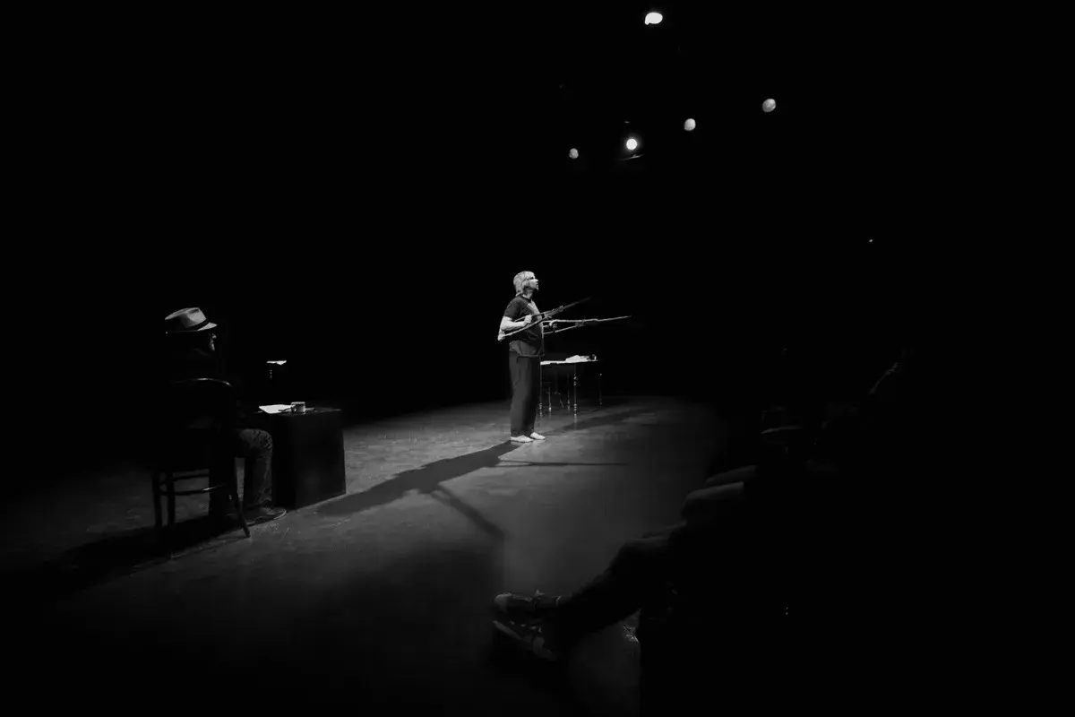 Na scenie Teatru Rondo w Słupsku kobieta z karabinami, mężczyzna w kapeluszu siedzi przy biurku.