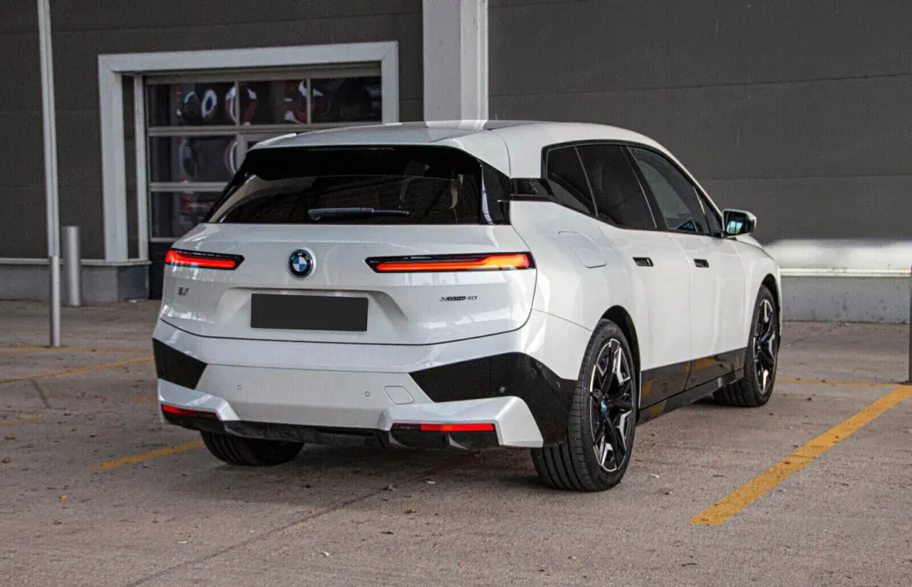 Białe BMW iX z czarnymi akcentami stoi na parkingu.
