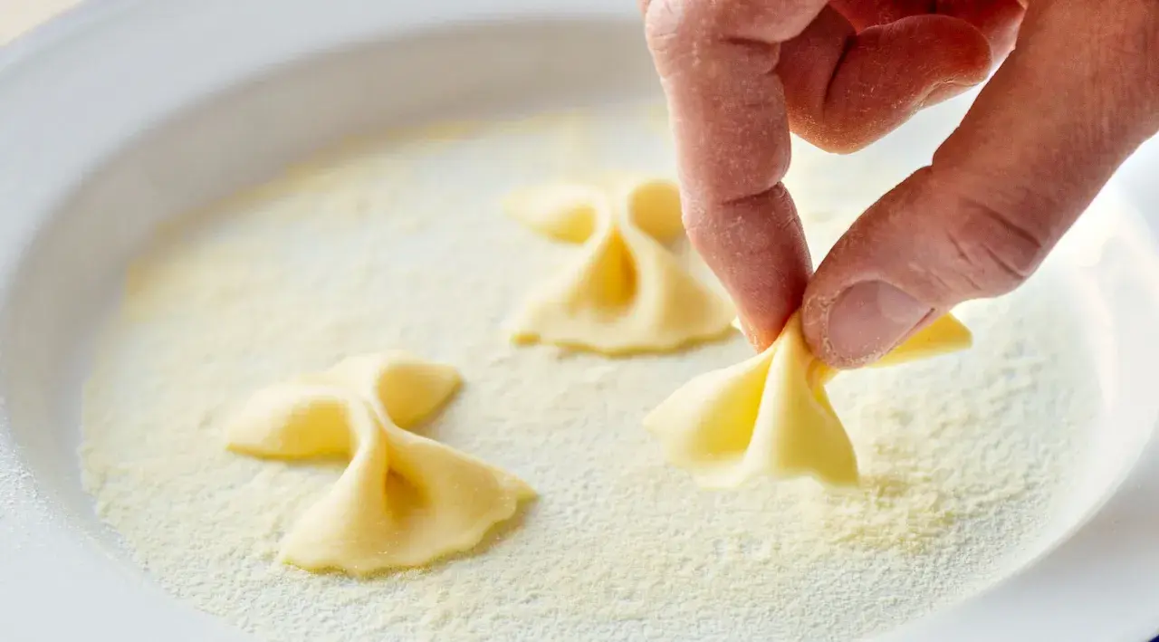 Hand formt Farfalle-Nudeln in einer Schüssel mit feiner farina di semola.