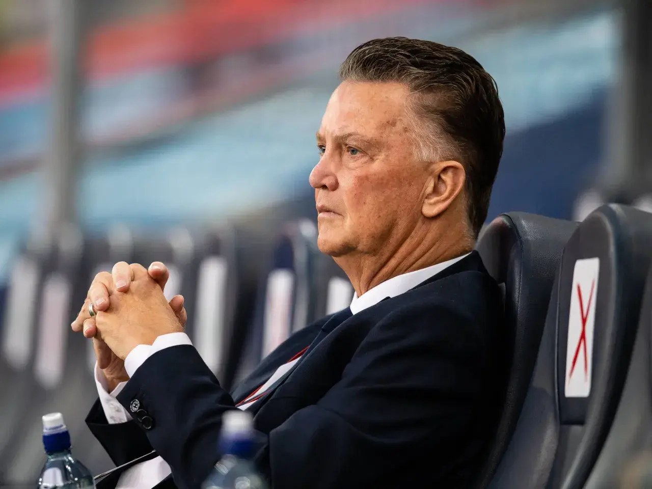 Louis van Gaal, znany z prowadzenia drużyny z pasją, siedzi z zamyślonym wyrazem twarzy, dłonie splecione.