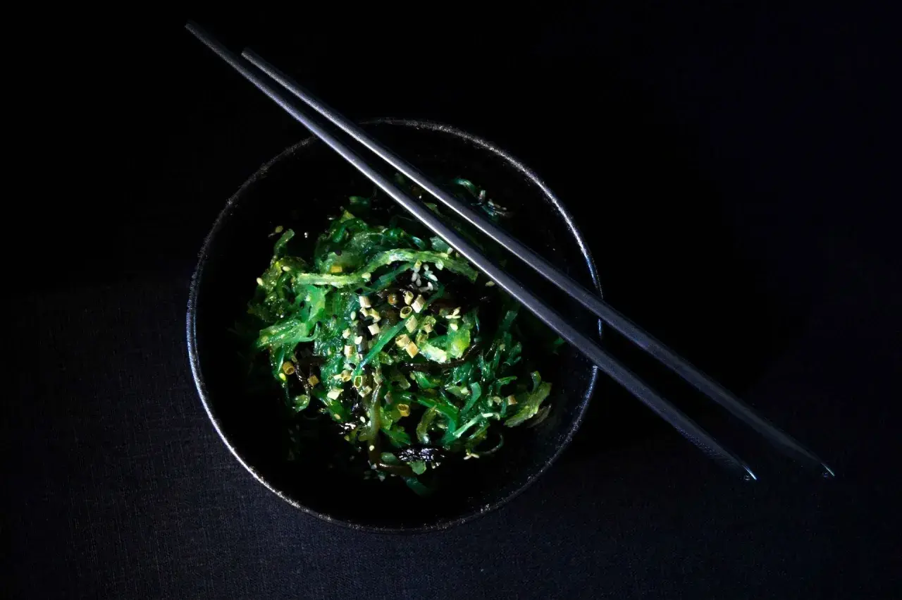 Insalata di wakame, un piatto ricco di **wakame proprietà** benefiche, guarnita con semi di sesamo e cipollotto, pronta per essere gustata con le bacchette.