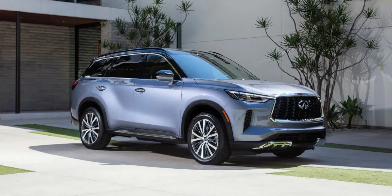 Elegancki, srebrny Infiniti QX60 parkuje przed nowoczesnym domem, otoczony bujną zielenią.