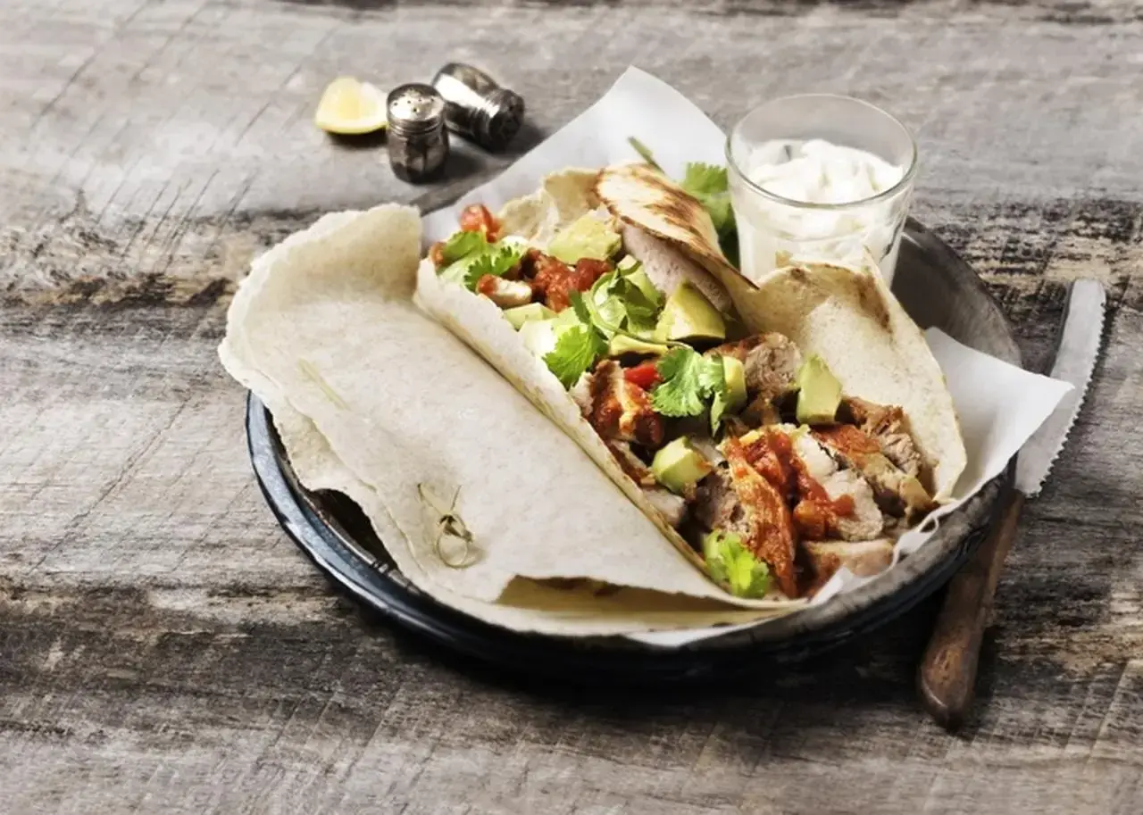 Tortilla z kurczakiem, awokado i sosem na drewnianym stole.