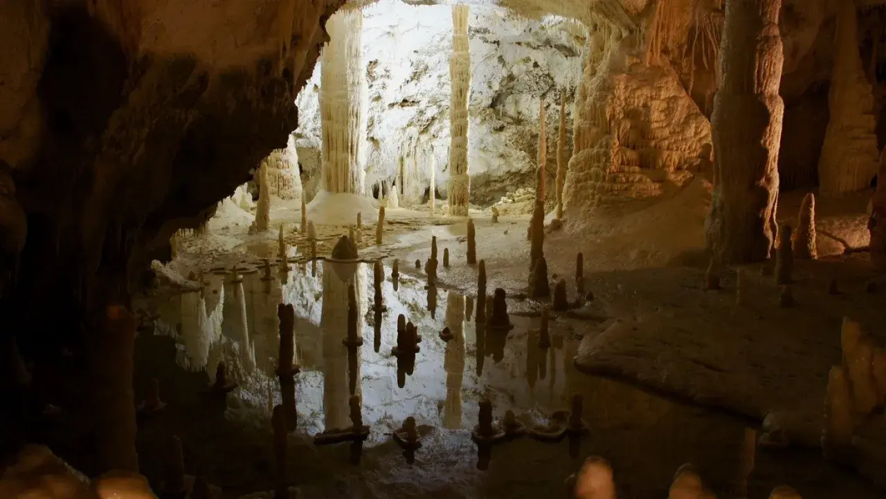 Stalattiti e stalagmiti riflettono in uno specchio d'acqua nelle grotte di Frasassi, dove si trovano meraviglie naturali.