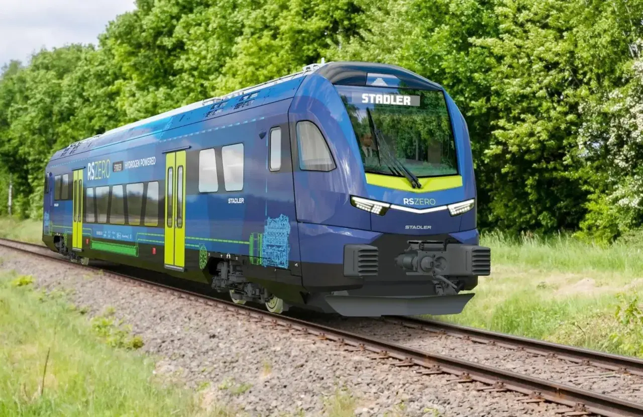 Niebieski pociąg Stadler RSZERO na wodór jedzie po torach wśród zieleni.