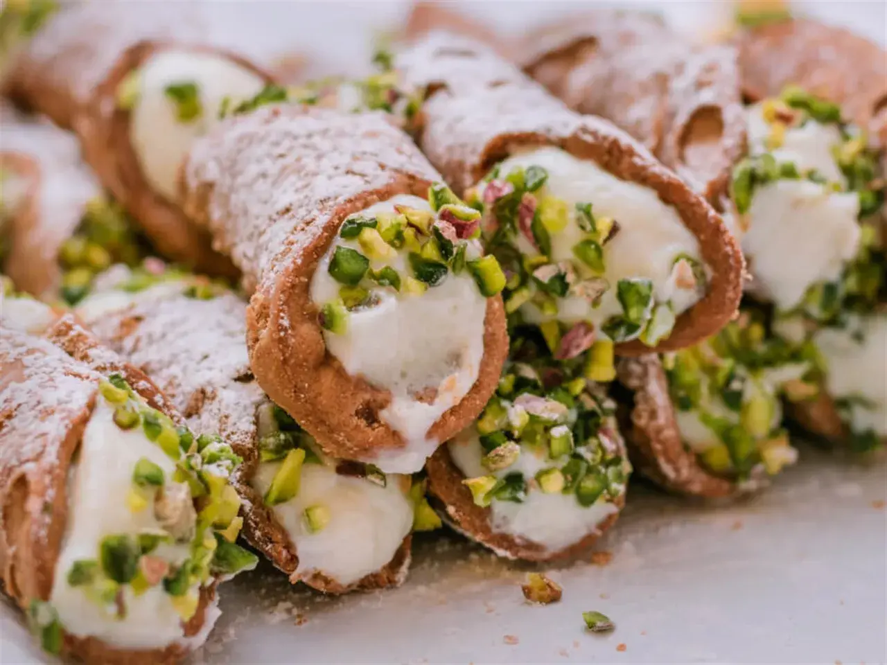 Stos delikatnych, włoskich rurek z kremem i pistacjami, posypanych cukrem pudrem.