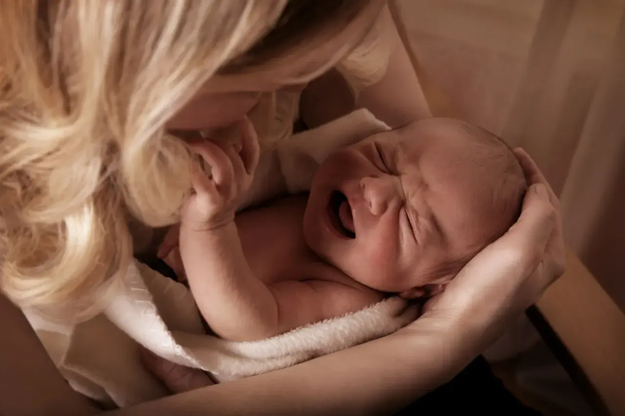 Matka tuli płaczące dziecko, szukając sposobu, jak odczynić urok na dziecku. Delikatne dłonie i włosy otulają maluszka.