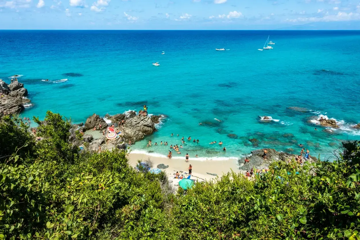 Spiaggia con acque cristalline e gente che nuota e prende il sole. Un luogo ideale per il tuo prossimo viaggio in Calabria mare dove andare.