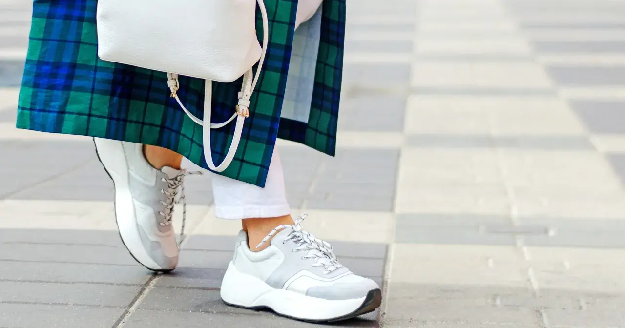 Stylowe białe sneakersy damskie idealnie komponują się z białą stylizacją i zielono-niebieską kraciastą marynarką.