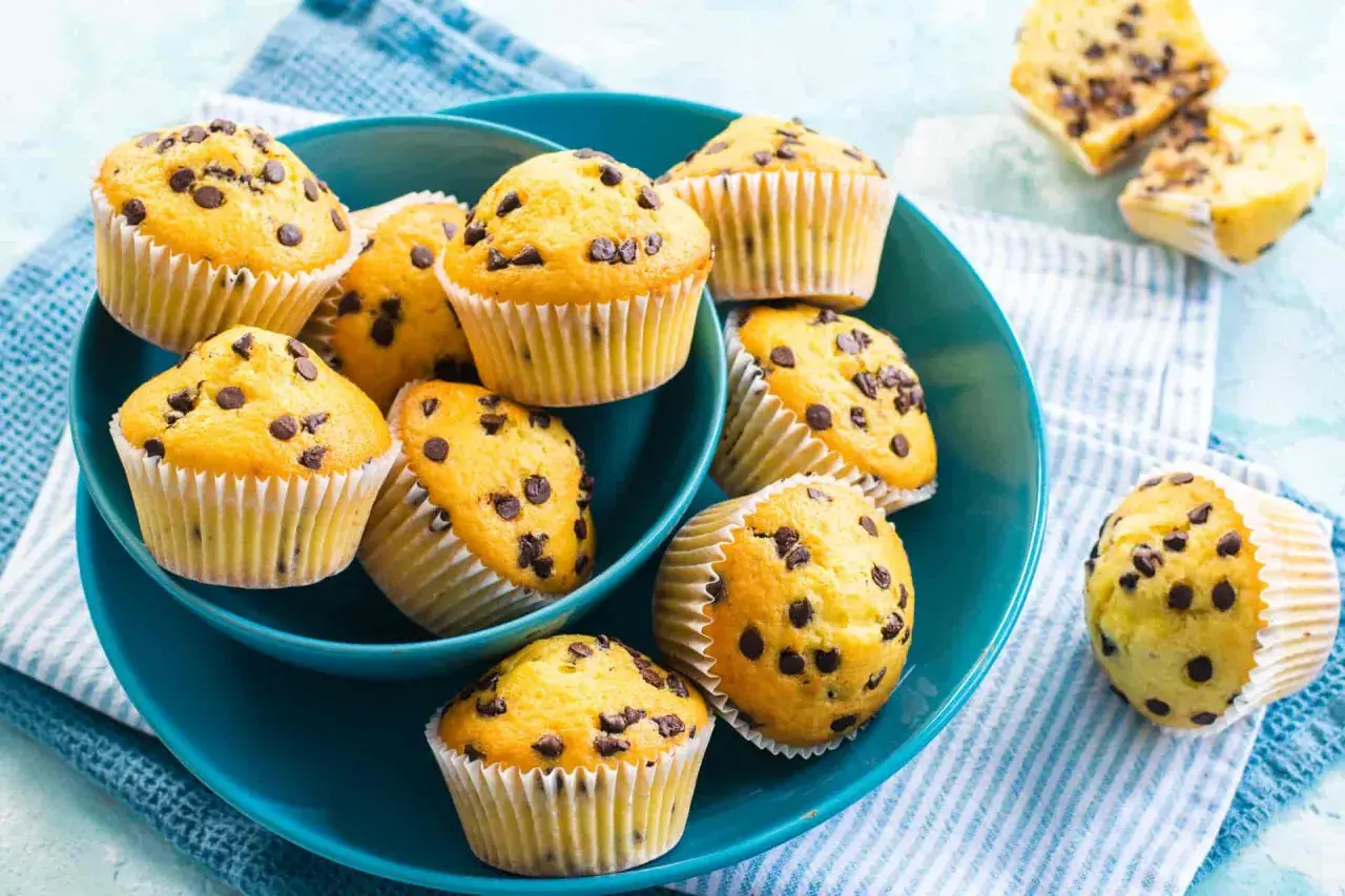 Muffin con gocce di cioccolato, dorati e invitanti, serviti in una ciotola blu. Perfetti per una pausa golosa.