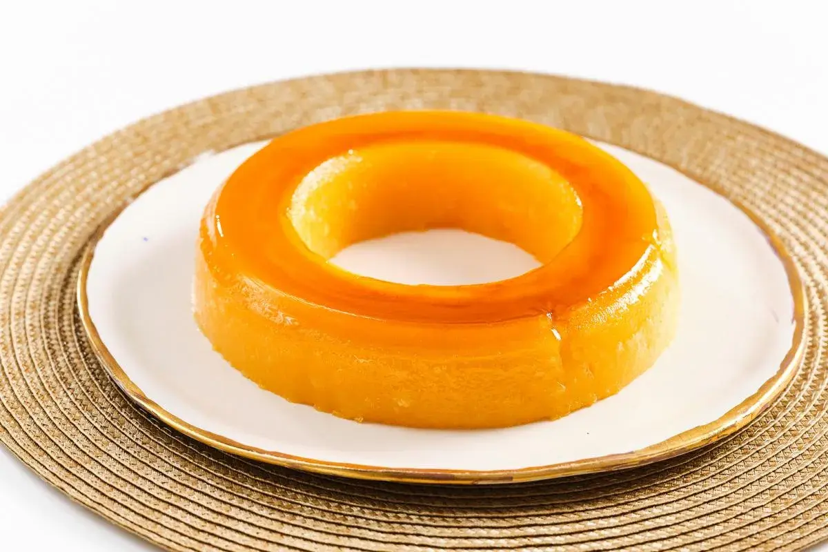 Un delicioso tocino de cielo, con su característico color dorado y forma de anillo, reposa sobre un plato blanco con borde dorado.