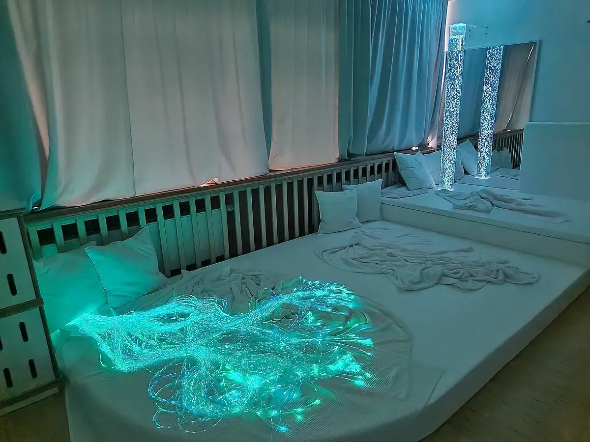 Ein beruhigender Snoezelen Raum mit weißen Matratzen, Kissen und faszinierenden Lichteffekten, darunter leuchtende Glasfasern.