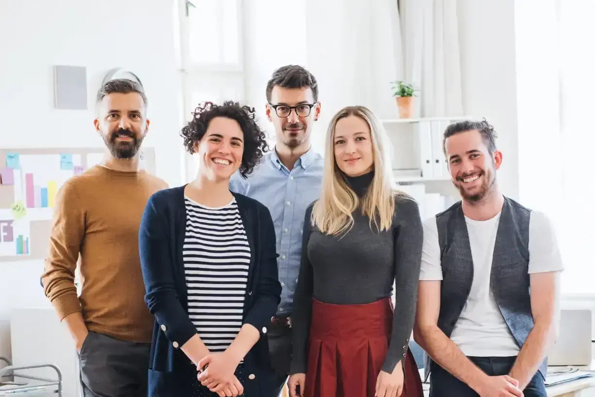 Fünf lächelnde Personen stehen im Büro. Sie haben erfolgreich ihr Fernstudium anerkannt und feiern ihren Erfolg.