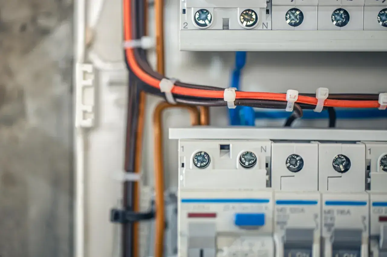 Profesjonalne wykonywanie instalacji elektrycznych: przewody w skrzynce rozdzielczej, bezpieczniki i zaciski.