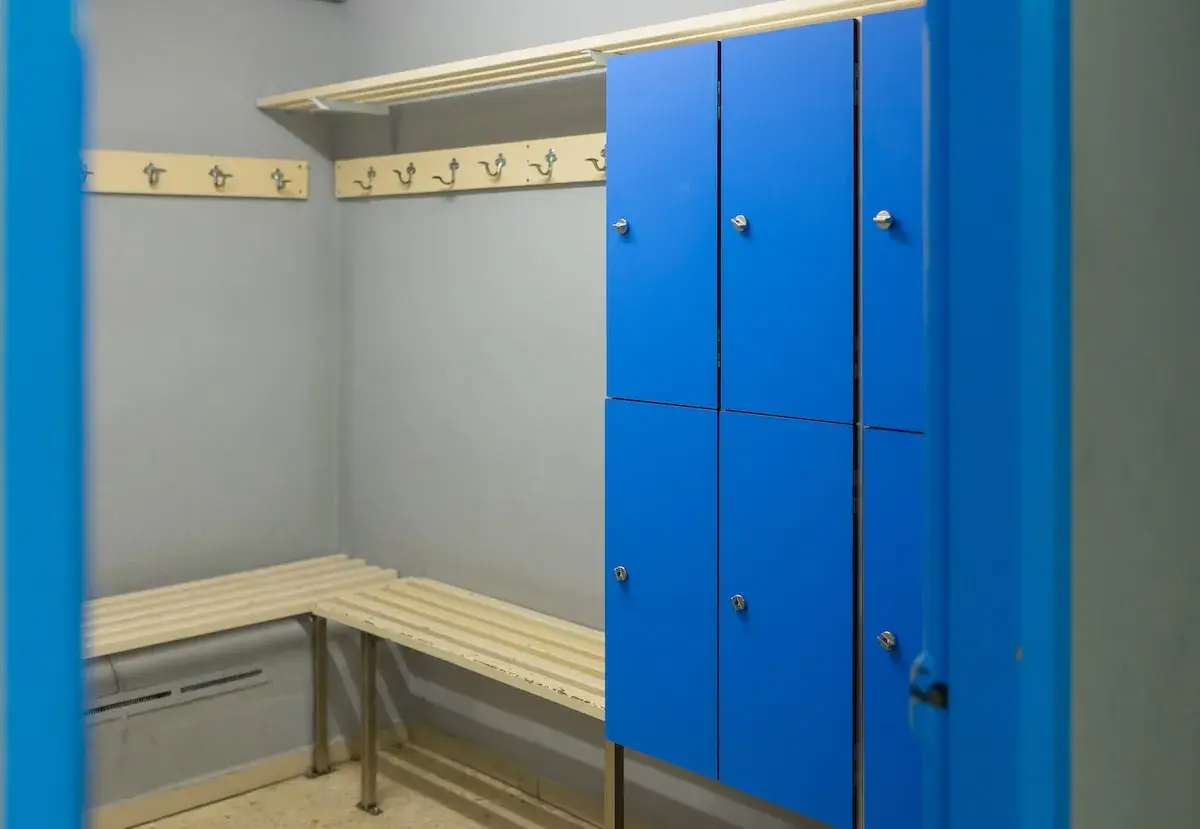 Un vestiaire avec des casiers bleus, des bancs en bois et des patères.