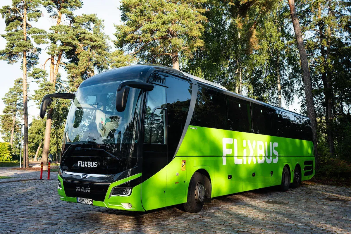Zielony autokar Flixbus zaparkowany na brukowanym placu, otoczony drzewami.