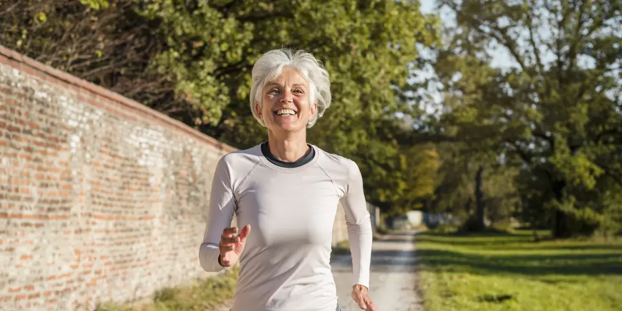 Femme souriante de 60 ans courant sur un chemin, suivant un plan d'entraînement course à pied.