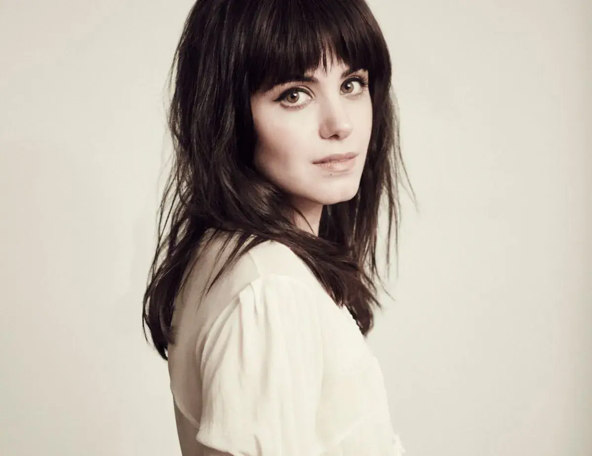 Katie Melua, jakby śpiewała "I Will Be There", z ciemnymi włosami i przenikliwym spojrzeniem.