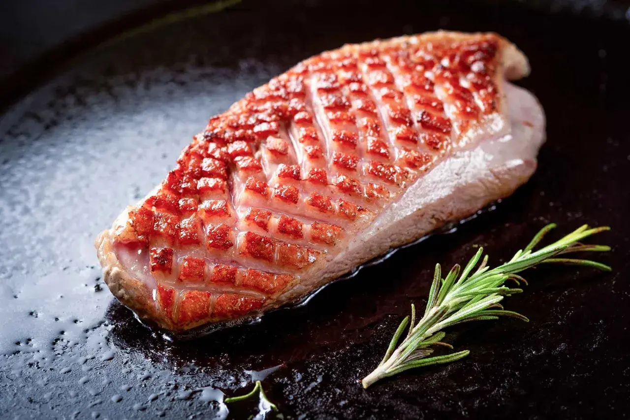 Magret de canard à la poêle, peau dorée et croustillante, avec une branche de romarin. Le temps de cuisson est idéal pour un plat savoureux.
