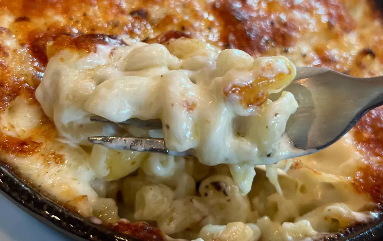 Un tenedor levanta una porción cremosa de macarrones con queso horneados, con la parte superior dorada y burbujeante.