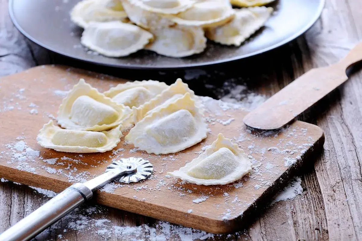 Raviolis frais sur une planche à découper avec une roulette à pâtisserie et une spatule.
