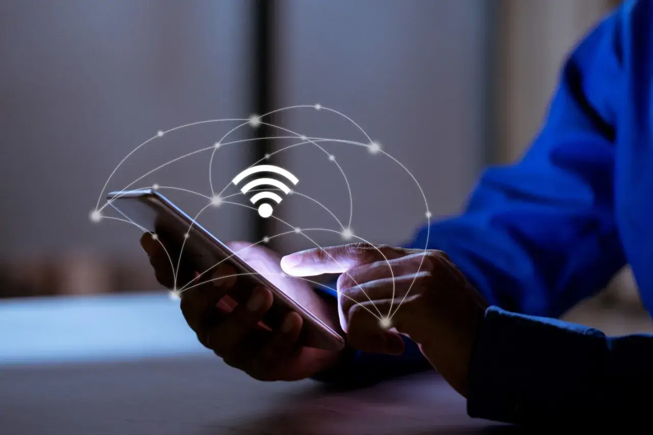 Dłoń dotyka ekranu smartfona, nad którym unosi się grafika symbolizująca sieć i sygnał Wi-Fi. To połączenie z apn plus.