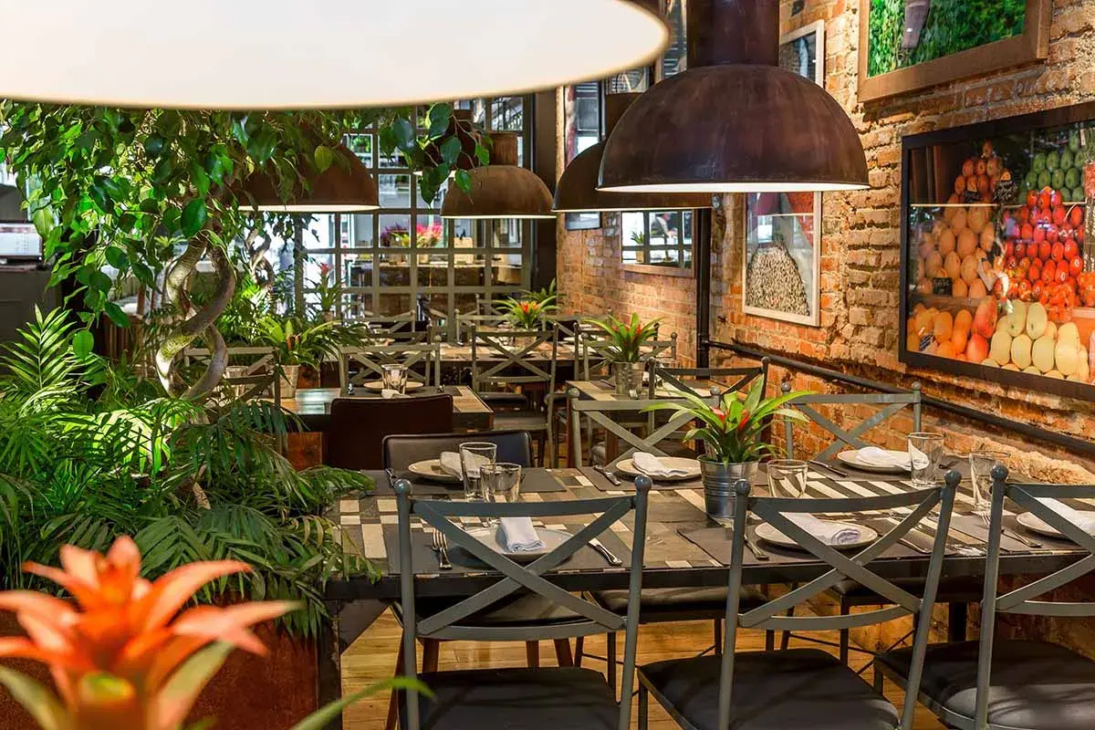 Tavoli apparecchiati in un ristorante con piante rigogliose e foto di frutta. Un'ottima opzione per sapere dove mangiare a Madrid.