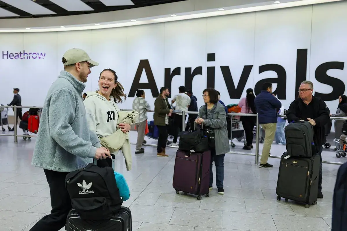 Para podróżnych z bagażami na lotnisku Heathrow, na tle napisu "Arrivals".