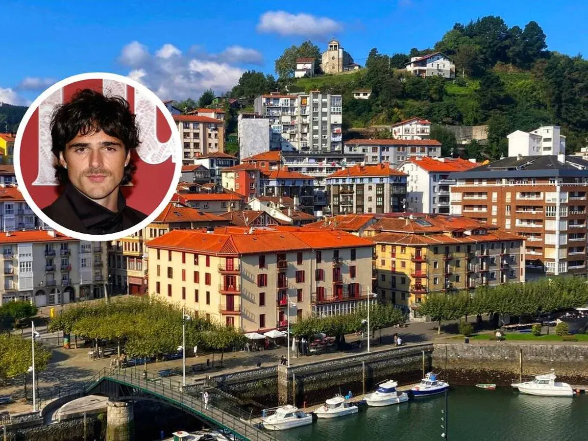 Jacob Elordi, con su aire de galán, posa sobre un pintoresco pueblo vasco con casas de tejados naranjas y un puerto lleno de barcos.