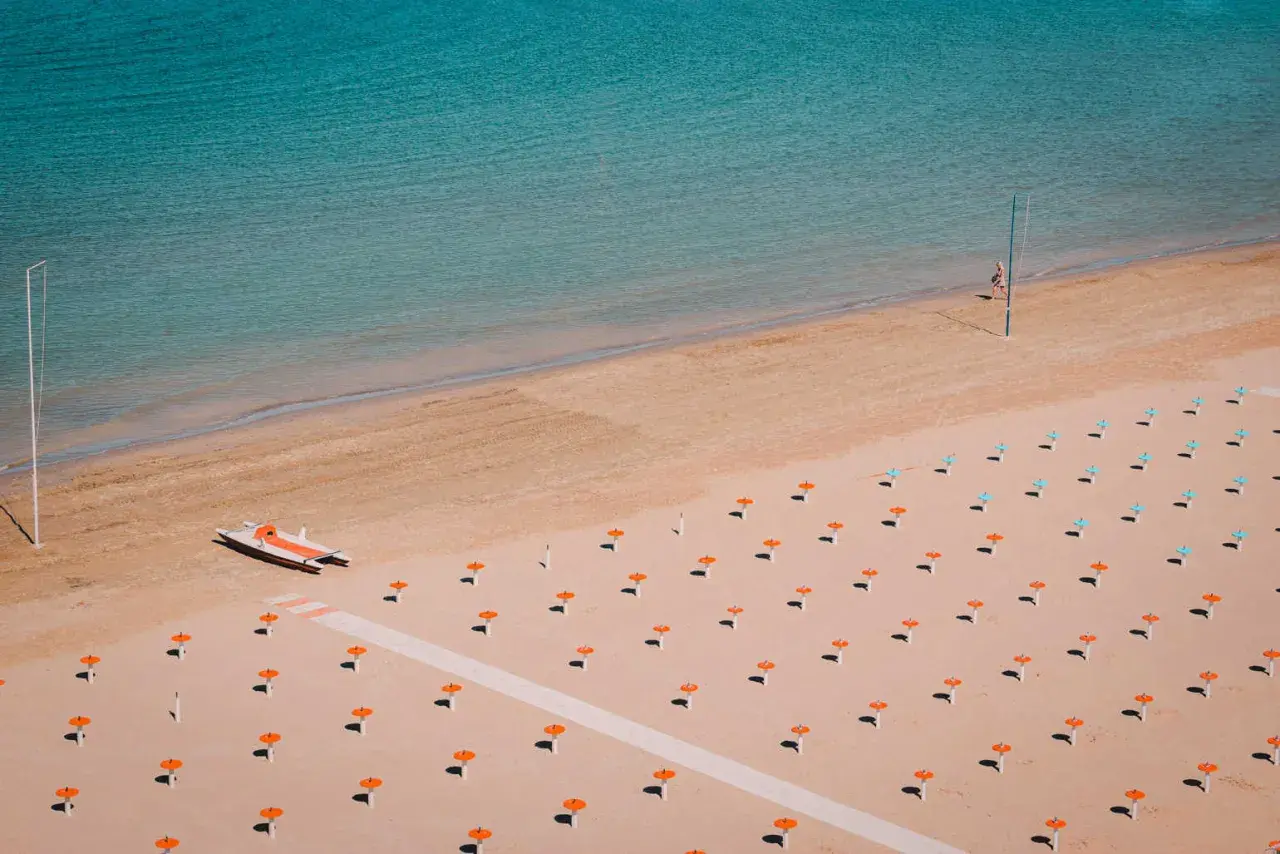 Pusta plaża w Rimini z rzędem pomarańczowych parasoli i małą łodzią motorową.