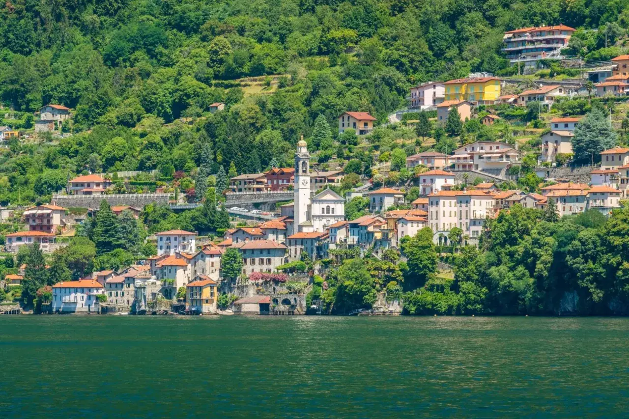 Ein malerisches Dorf am Nesso Comer See, mit traditionellen Häusern, die sich an den grünen Hang schmiegen.