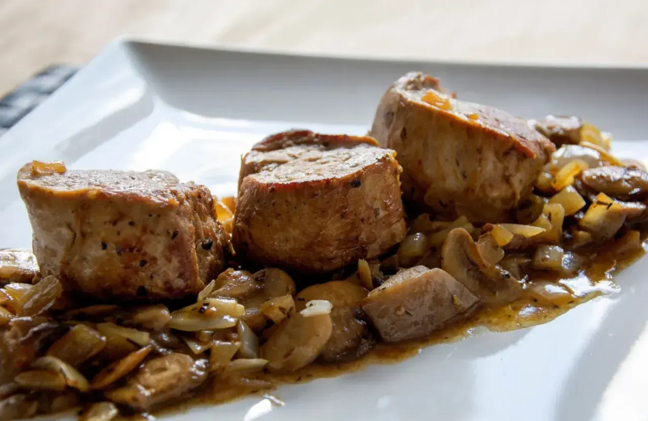 Soczyste polędwiczki w sosie pieczarkowym, podane na białym talerzu. Aromatyczny sos z pieczarkami i cebulką otula delikatne mięso.
