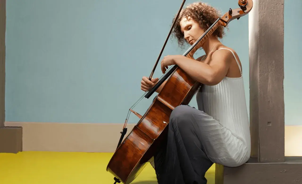 Une jeune femme aux cheveux bouclés s'applique à apprendre le violoncelle, concentrée sur son instrument.