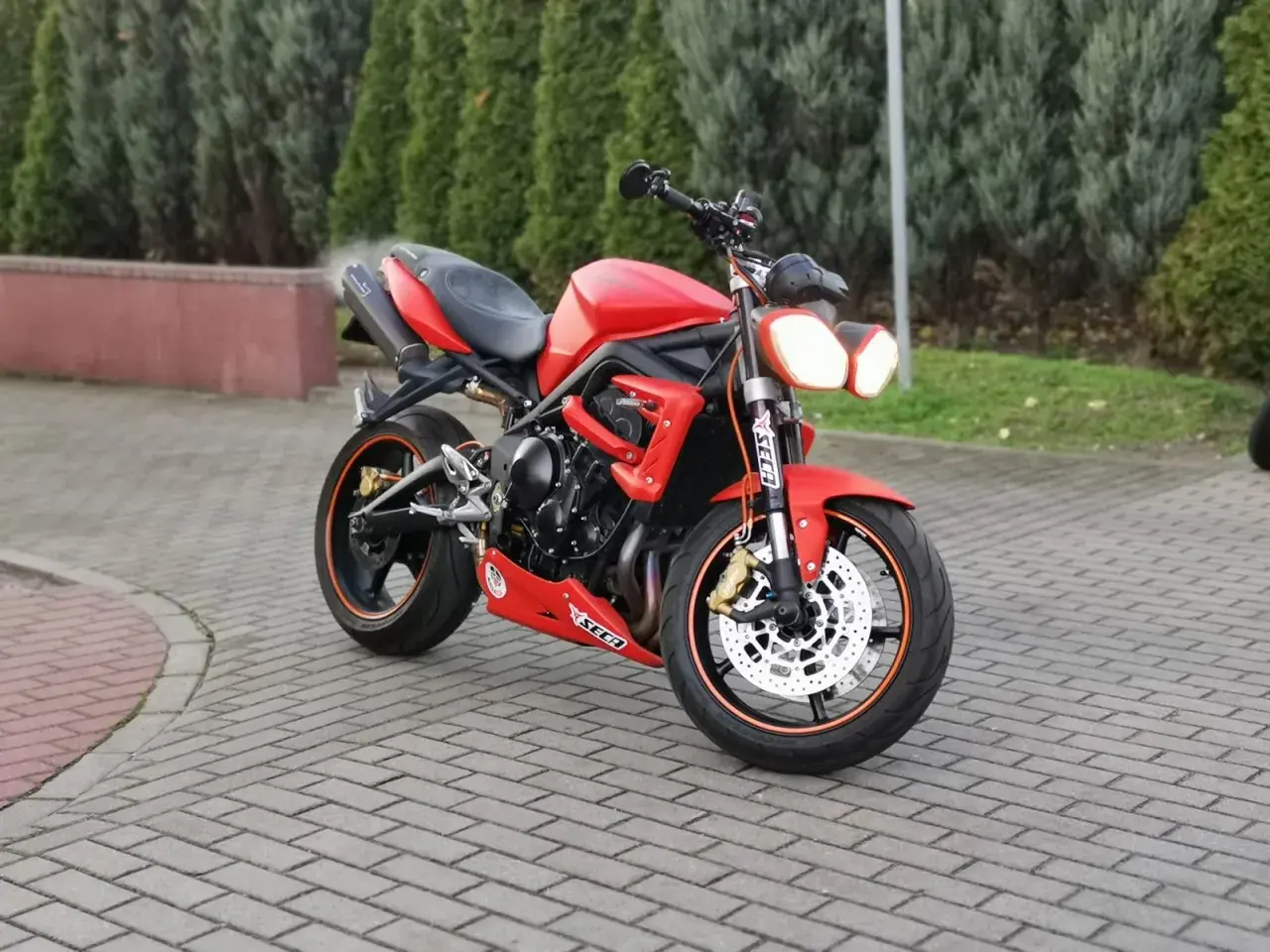 Czerwony motocykl Triumph Street Triple 675 na brukowanym podjeździe.