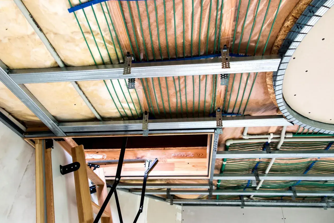 Widok sufitu podwieszanego z widocznymi instalacjami. Widać metalowe profile, wełnę mineralną, rurki systemu ogrzewania podłogowego i elementy konstrukcyjne. Maty kapilarne wady nie są widoczne.