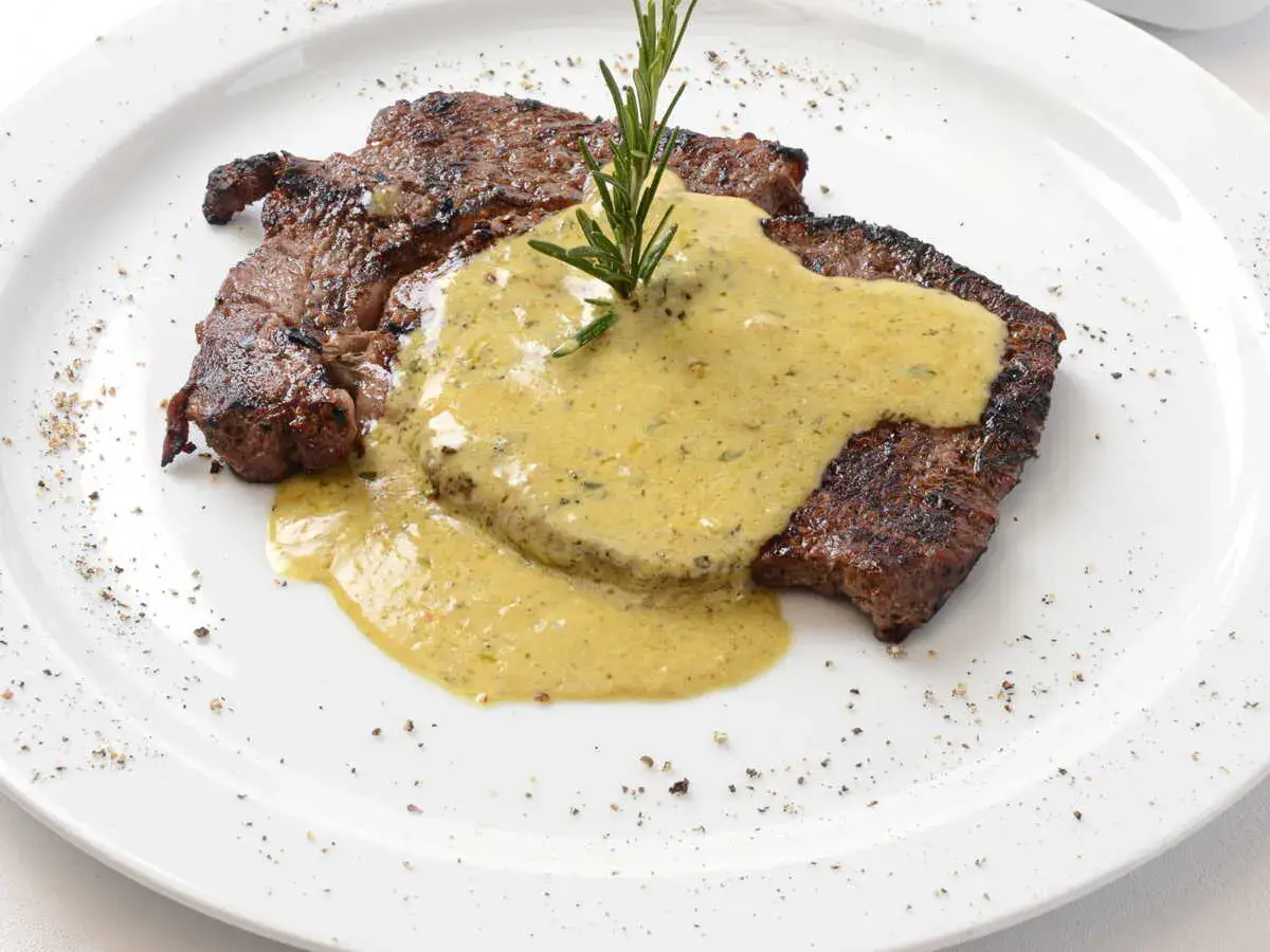 Un steak grillé, nappé d'une sauce crémeuse et garni d'une branche de romarin. Parfait pour accompagner une sauce pour entrecôte au barbecue.