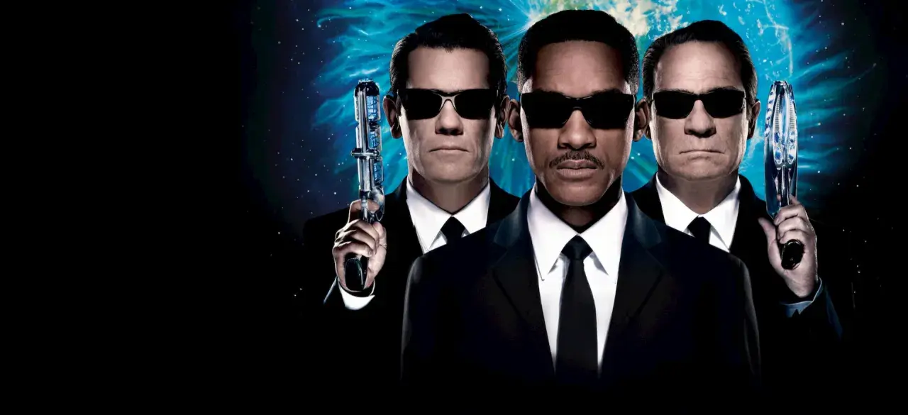 Agent J, K och O, rollistan i Men in Black 3, redo för action med sina futuristiska vapen mot en stjärnklar bakgrund.