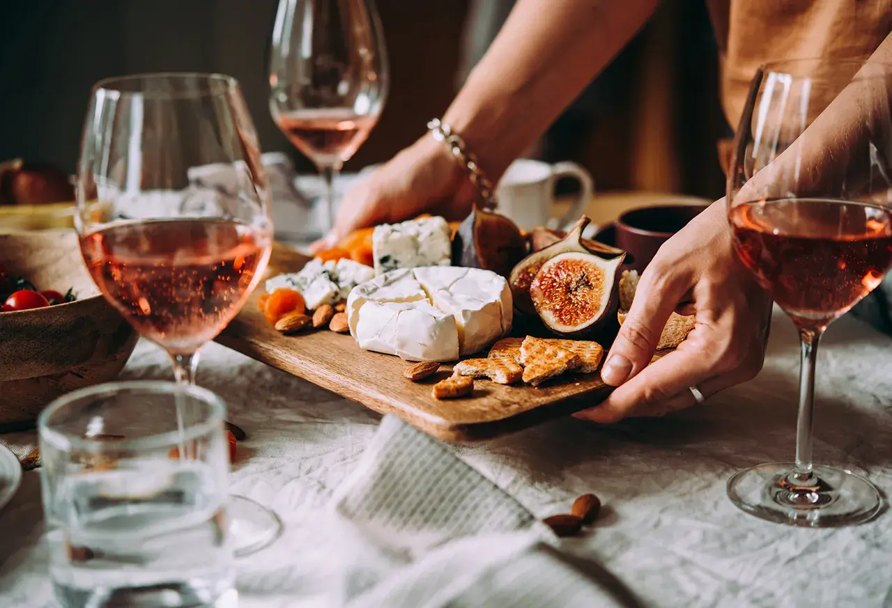 Gemütliche weinverkostung zu hause mit Roséwein, Käse, Feigen und Nüssen auf einem Holzteller.