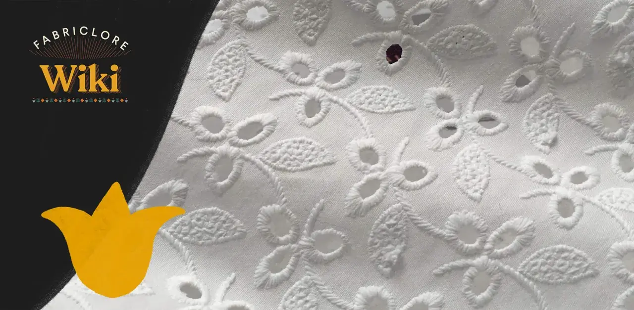 Close-up of white eyelet fabric with floral embroidery. This delicate fabric features cut-out holes surrounded by decorative stitching, creating a beautiful, airy pattern.