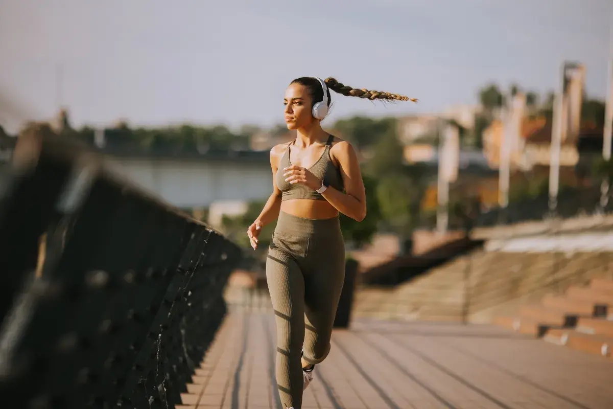 Donna con cuffie corre 10 km su un ponte, concentrata e determinata, con la treccia che ondeggia al vento.