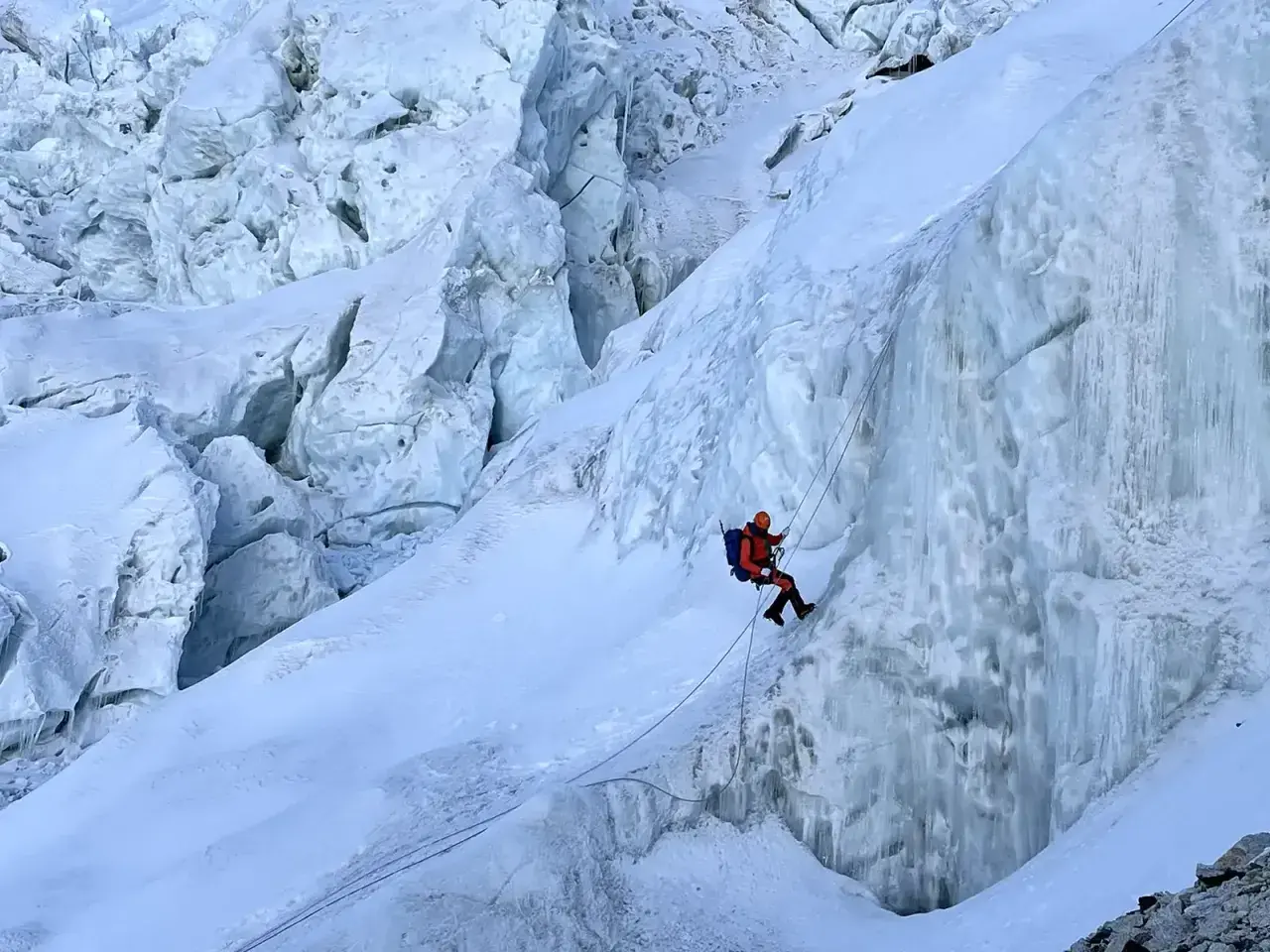 Bergsteiger seilt sich im Khumbu Icefall ab, umgeben von zerklüftetem Eis und tiefen Gletscherspalten.