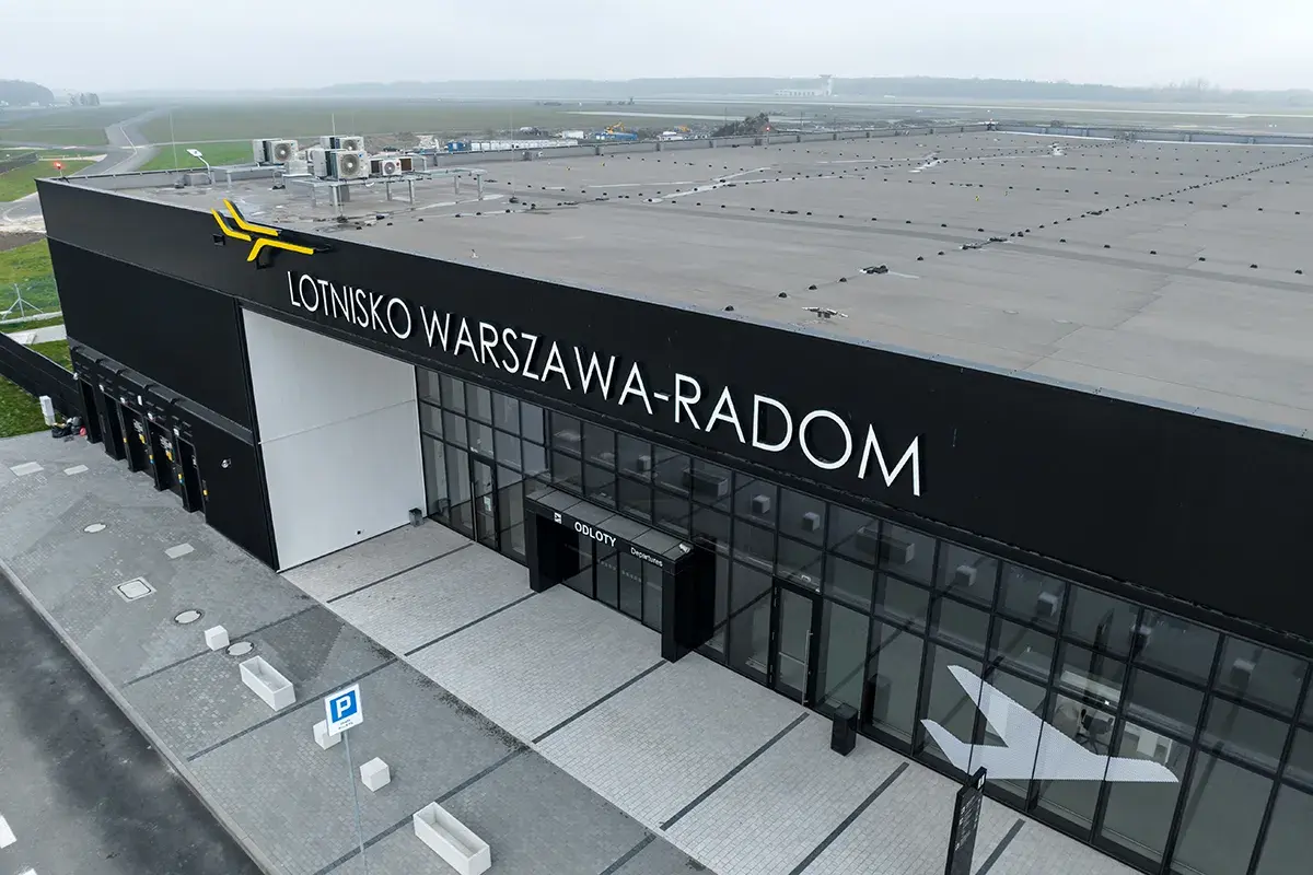 Nowoczesny budynek lotniska Warszawa-Radom z napisem "ODLOTY" i symbolem samolotu na szkle.