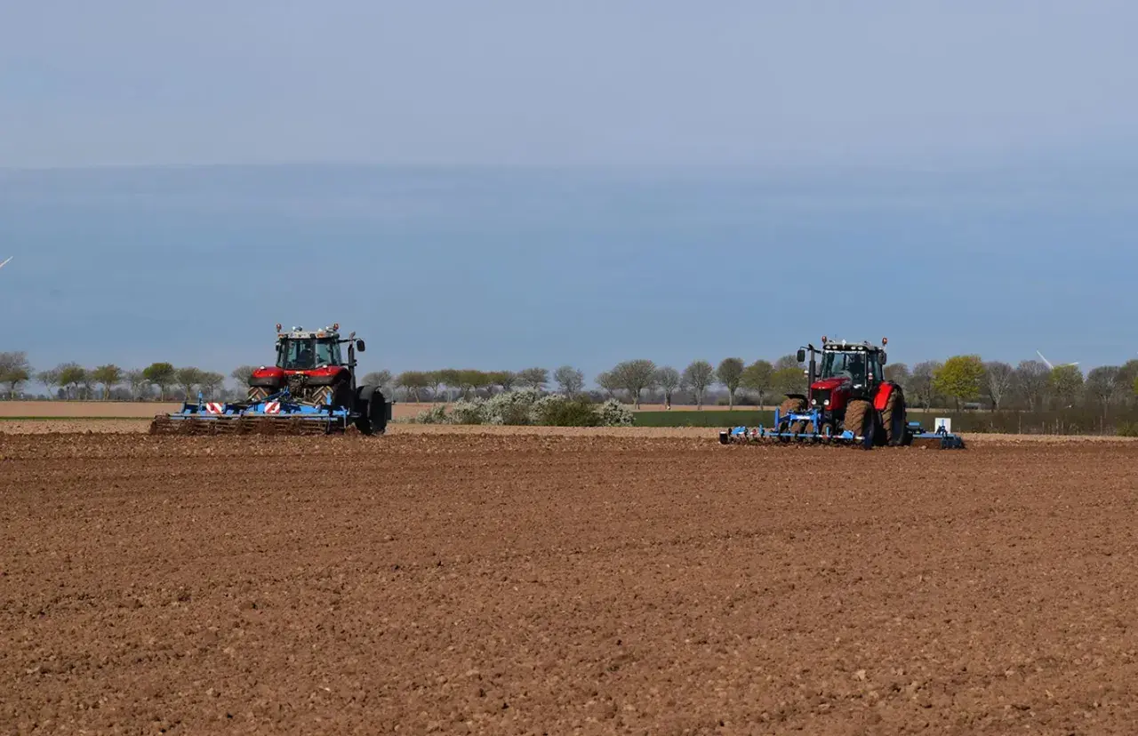 Deux tracteurs préparent le sol pour la culture du lin. Le champ est labouré, prêt pour les semis.