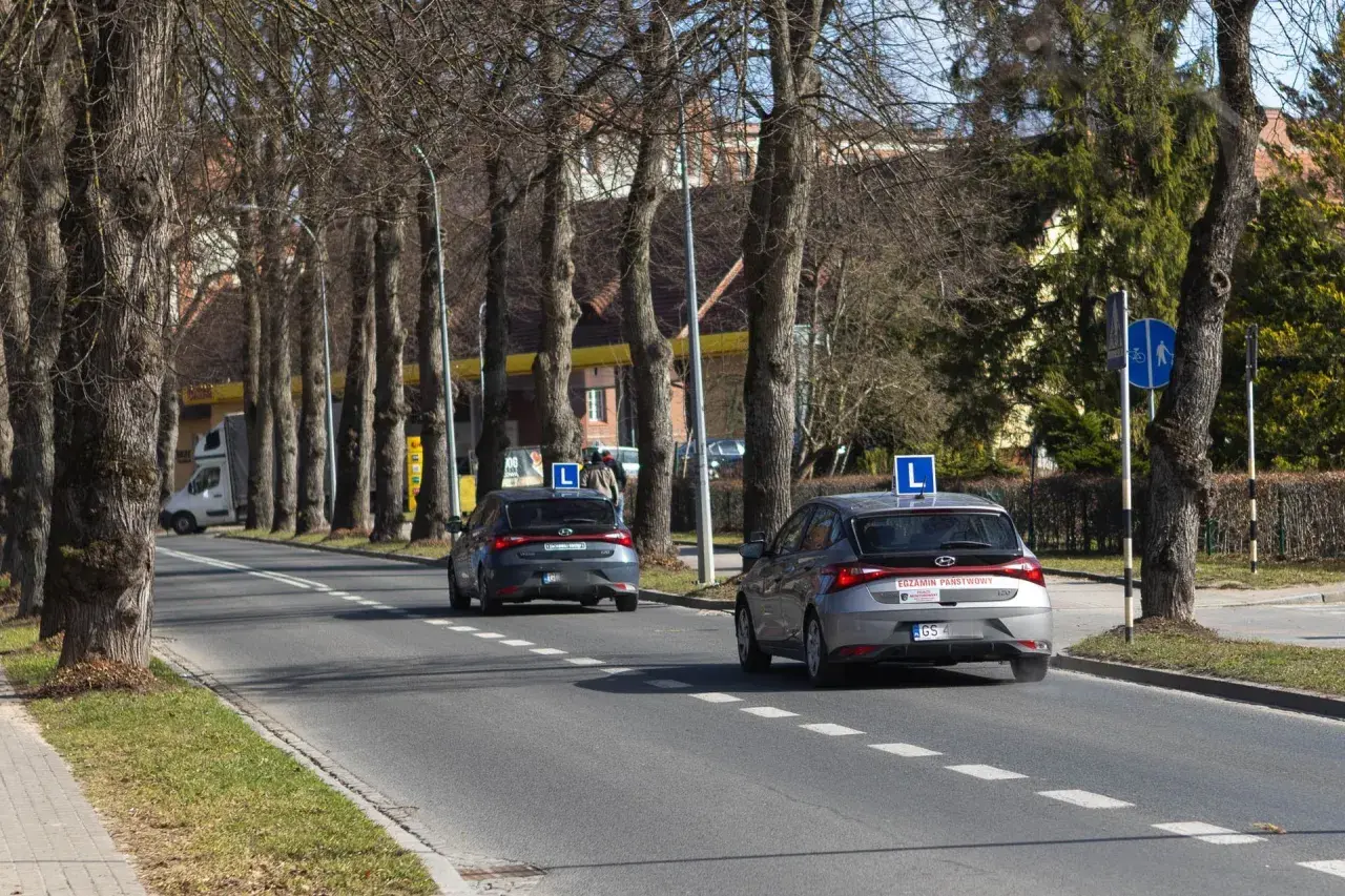 Dwa samochody z literą "L" na dachu, przygotowujące się do egzaminu praktycznego na prawo jazdy. Zastanawiasz się, ile kosztuje egzamin praktyczny na prawo jazdy?