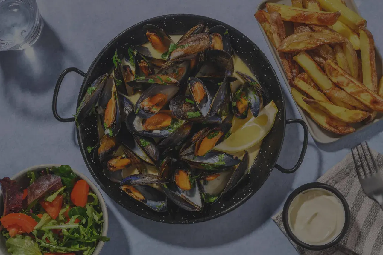 Un plat de moules frites, accompagné d'une salade fraîche et d'une sauce crémeuse. Un délice pour les amateurs de fruits de mer.