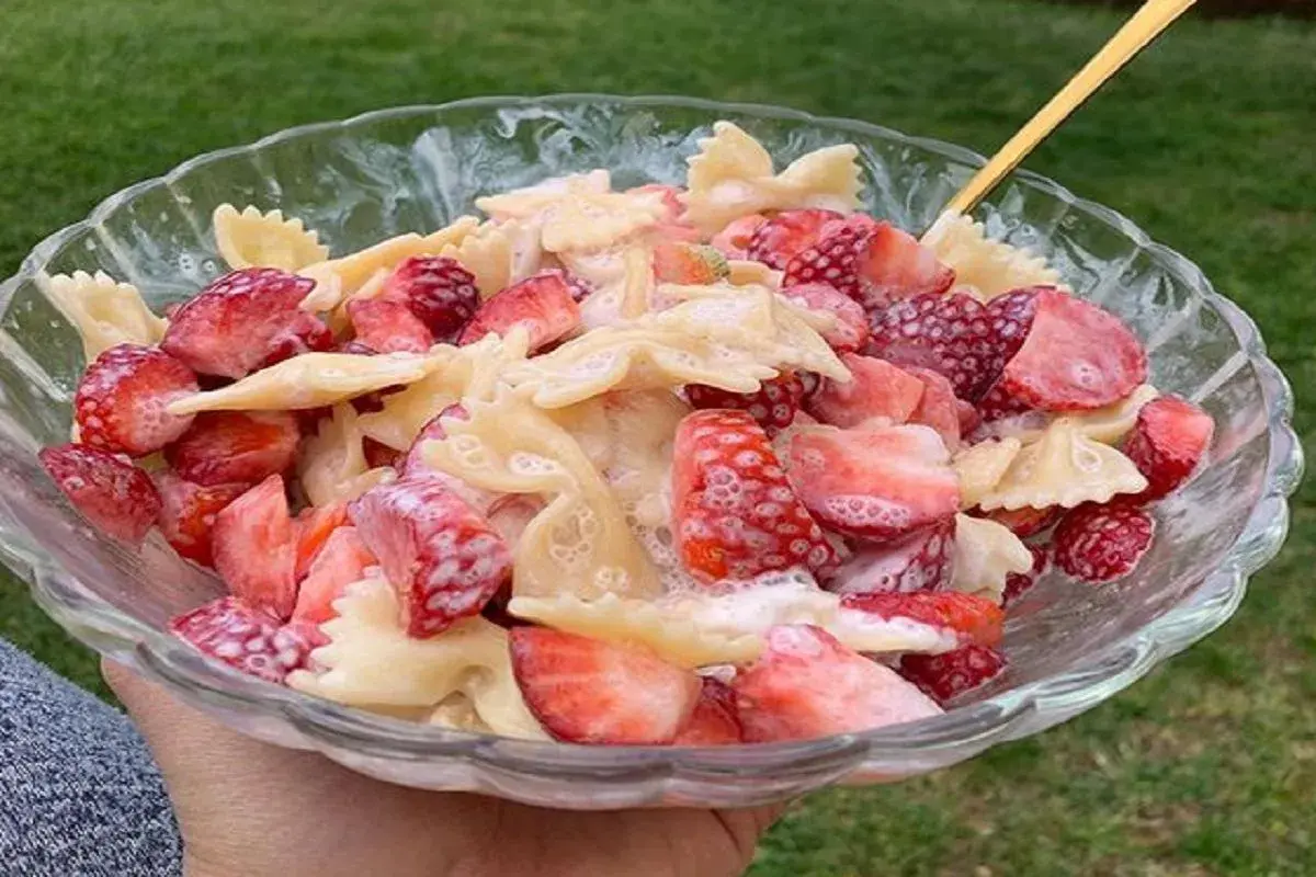 Makaron farfalle z kawałkami świeżych truskawek, polany kremowym sosem. Letnia uczta w misce.